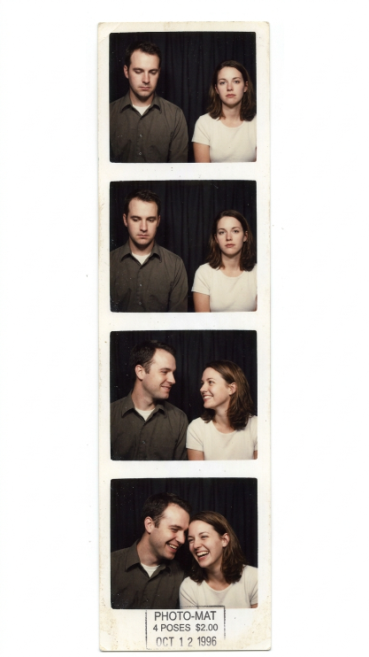 Create a vintage 1990s-style photo booth strip showing four small photos of the uploaded couple. In the first two frames they look like strangers standing awkwardly apart. In the third frame they begin to smile at each other. In the fourth frame they are laughing together naturally. Add realistic photo booth grain, soft flash lighting, white border edges, and nostalgic 1990s color tones.
